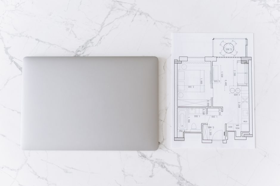 Top view of a laptop and architectural blueprint on white marble surface, showcasing modern workspace.