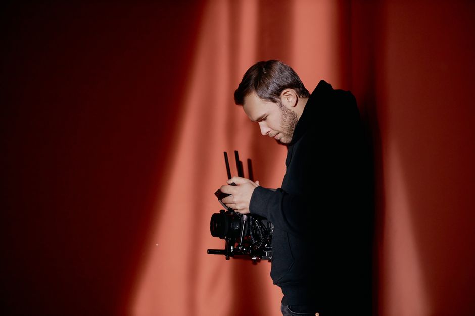 A focused videographer adjusting his professional camera against a red background.