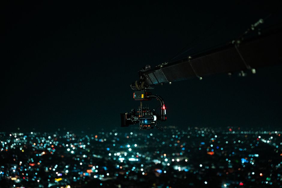 A cinematic drone camera captures a vibrant Indian cityscape at night.