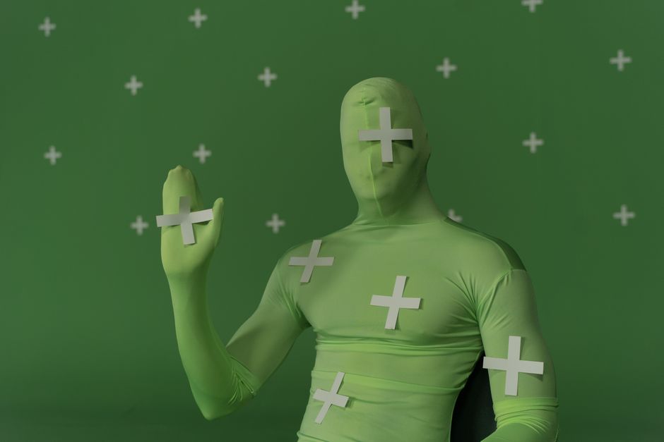 Person wearing a green screen suit with tracking markers for visual effects work.