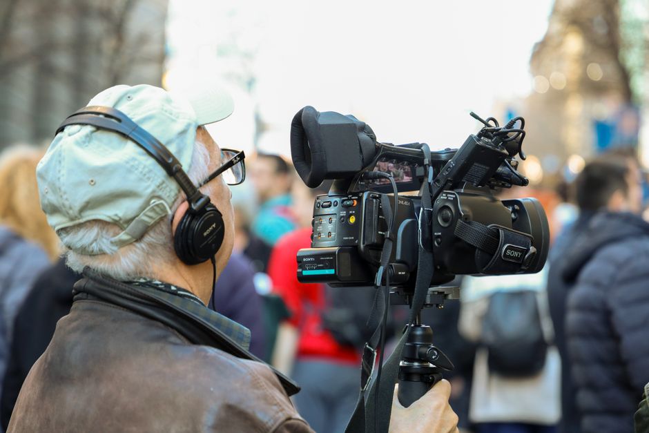A cameraman records an urban event with professional equipment in a bustling city setting.