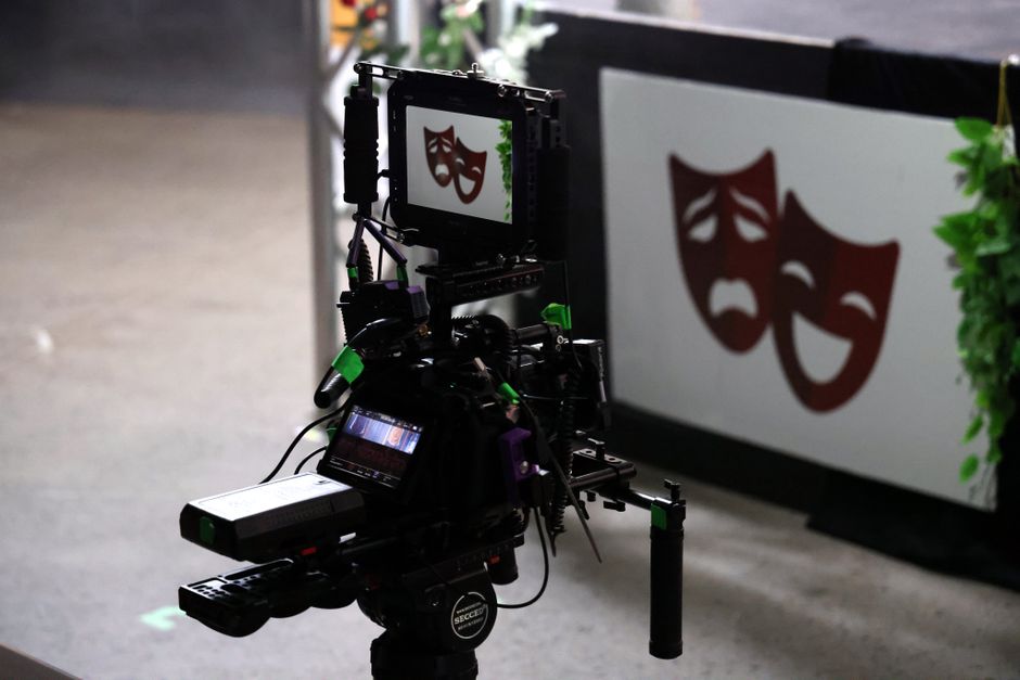 Professional film camera capturing theater performance showing drama and comedy masks.