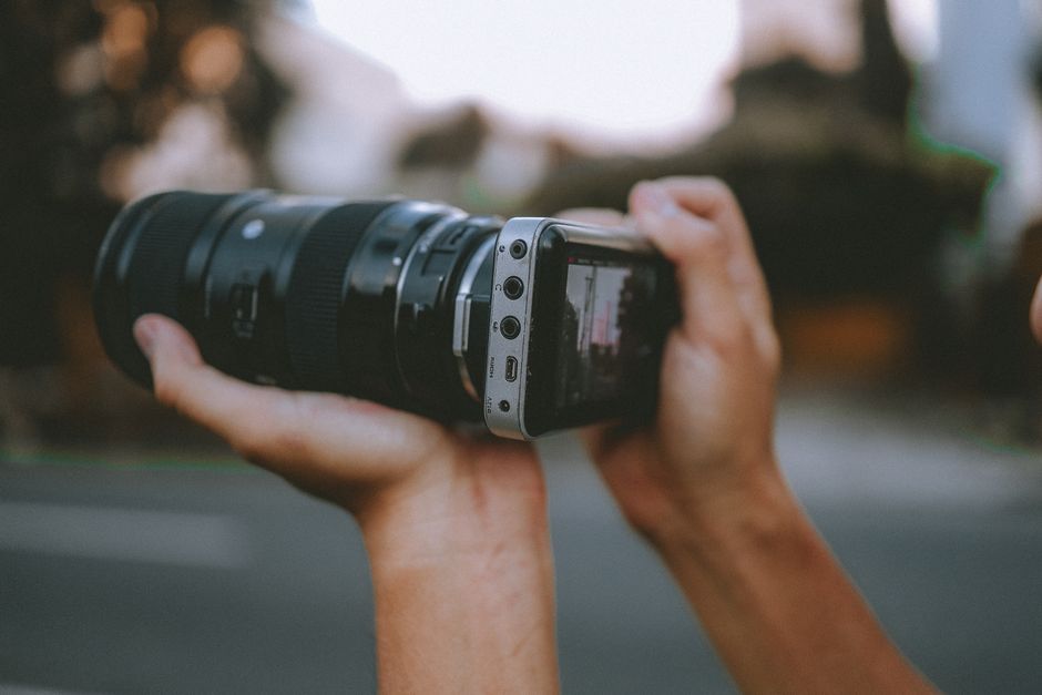 Hands holding a smartphone camera adapter with lens outdoors.