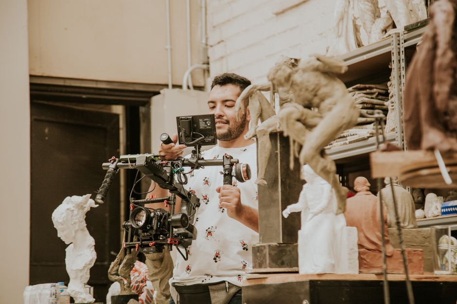 A man using a video camera to capture art sculptures in a studio setting.