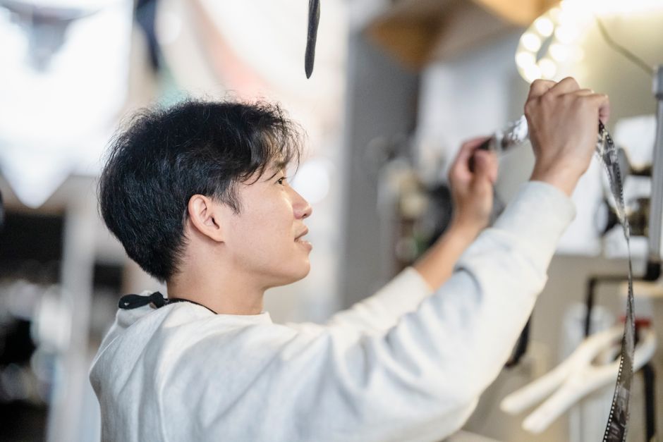 Asian male photographer developing film in a darkroom setting, focusing on detail and technique.