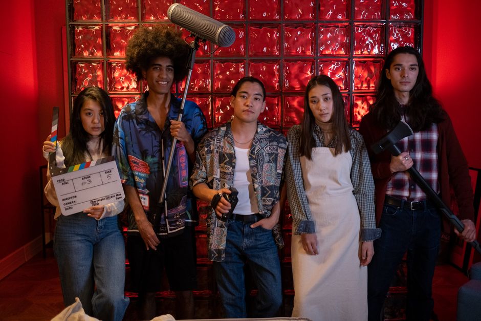 A diverse group of five people standing with film equipment indoors. Creative scene with vibrant red background.