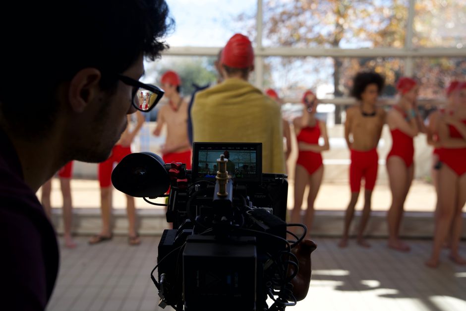 Behind-the-scenes view of a cameraman recording a swim team indoors.