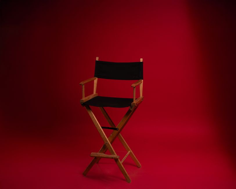 A wooden director's chair against a vibrant red backdrop, symbolizing film industry authority.