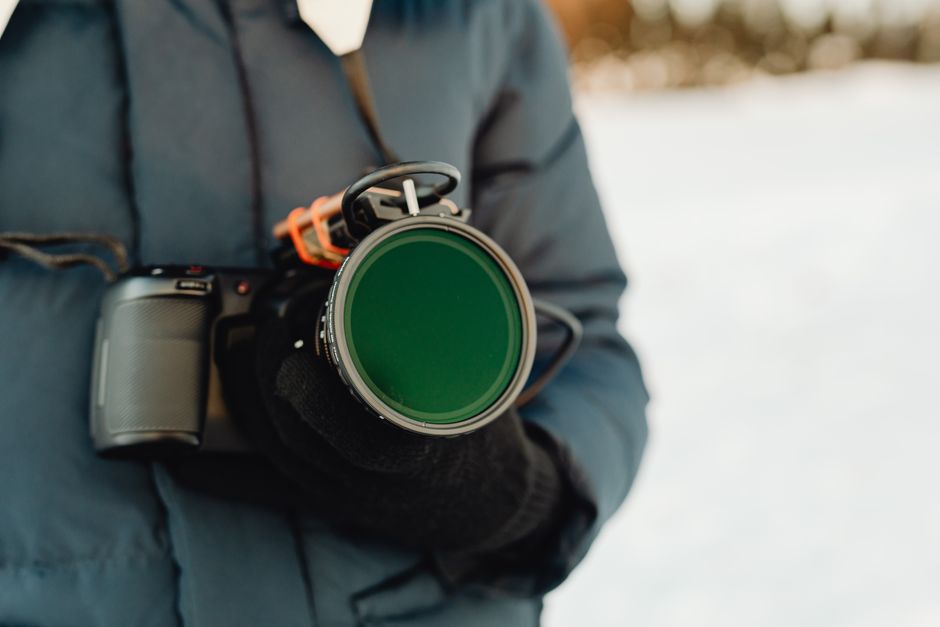 Close-up of a photographer holding a camera with a lens outdoors during winter.