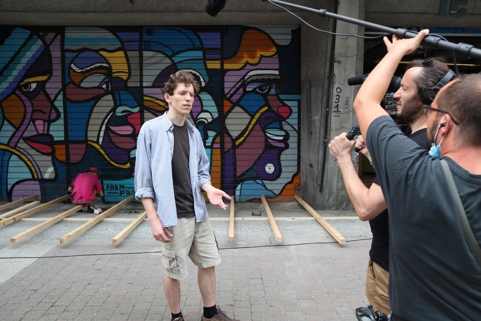 A man conducting an interview in front of a vibrant street mural.