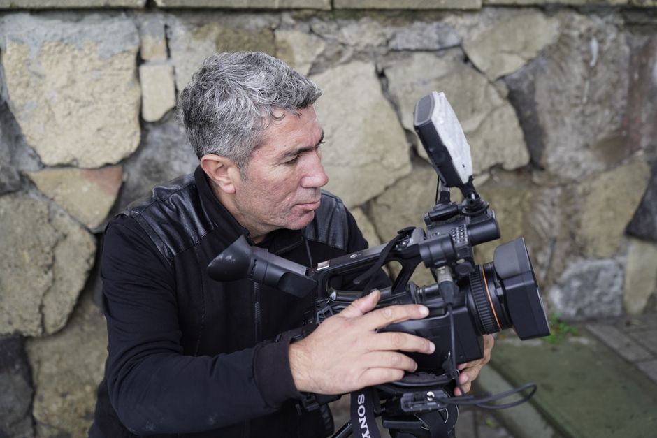Experienced filmmaker adjusting a professional video camera outdoors.