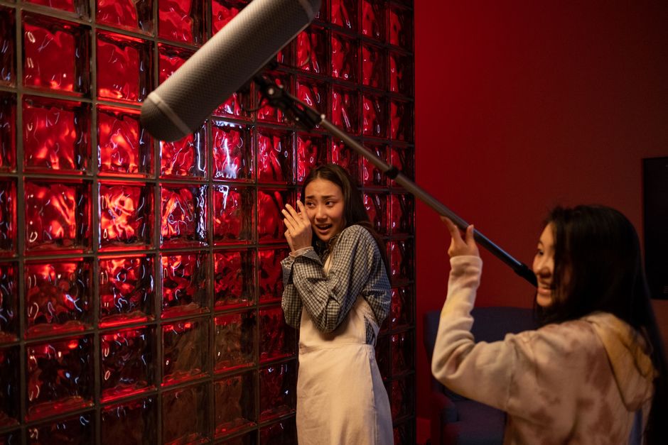 Two teenagers act out a dramatic movie scene with a microphone setup indoors.