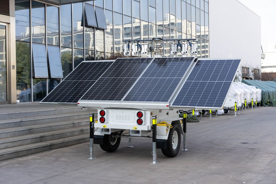 A mobile solar panel trailer parked outdoors by a modern building, showcasing renewable energy technology.