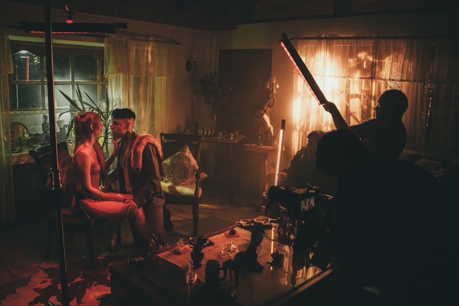An intimate indoor setting with warm, moody lighting and a couple seated amidst filming equipment.
