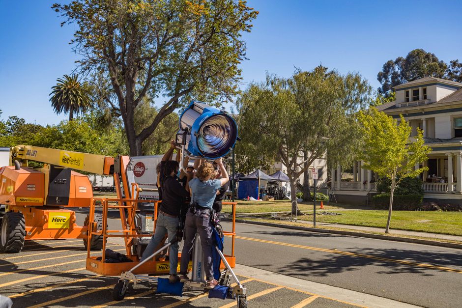 Film crew setting up lighting equipment outdoors on location shoot.