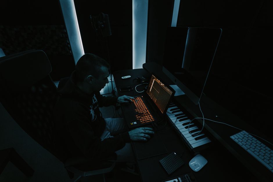 Man working on audio production in a dimly lit studio with multiple screens and equipment.