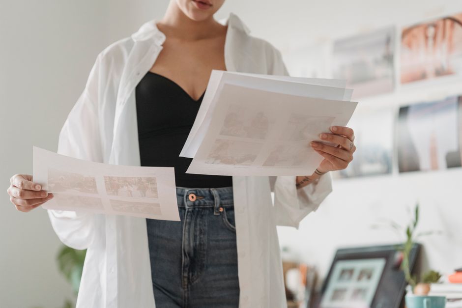 Crop anonymous female employee comparing photos on paper sheets while working on project in light house