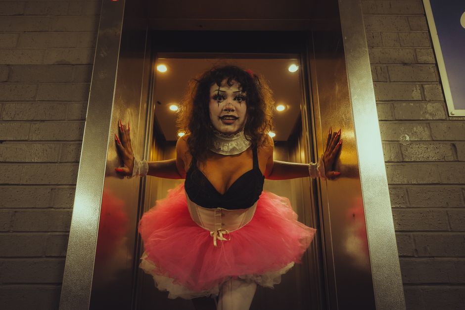 A person in clown makeup and tutu costume emerging from an elevator, showcasing gothic and horror aesthetics.