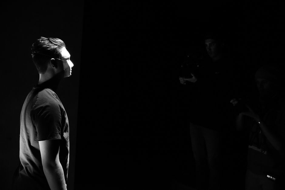 A moody black and white portrait of a man in a spotlight, with a dark background and dramatic lighting.