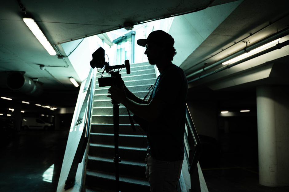 Silhouette of a filmmaker holding a camera in an underground parking area with stairs.
