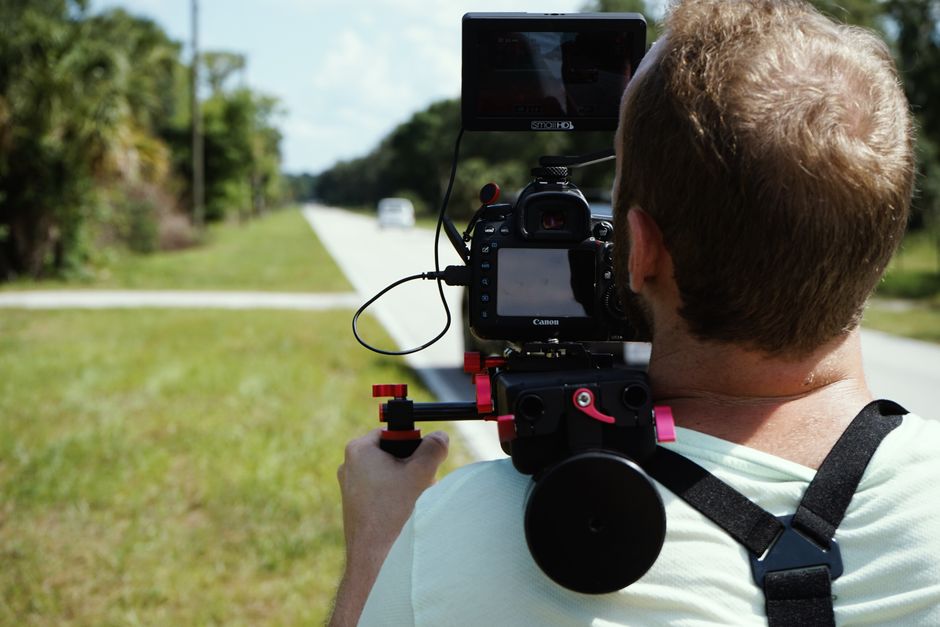 Videographer using a shoulder-mounted camera to film outdoors on a sunny day.