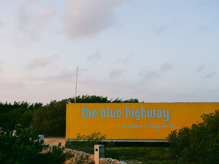 Yellow billboard with 'the blue highway' text against serene outdoor backdrop.