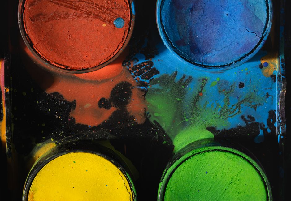 A close-up of a colorful paint palette showing vibrant pigments in red, blue, yellow, and green.