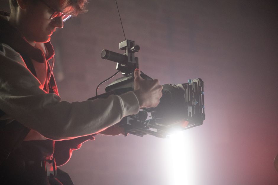 Cameraman using an Easyrig to film in a dimly lit studio with spotlight effects.