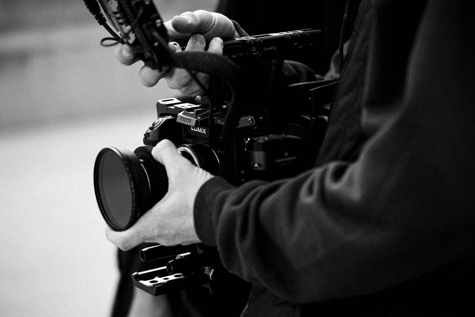 Monochrome close-up of a professional camera being handled, with detailed view of controls and lens.