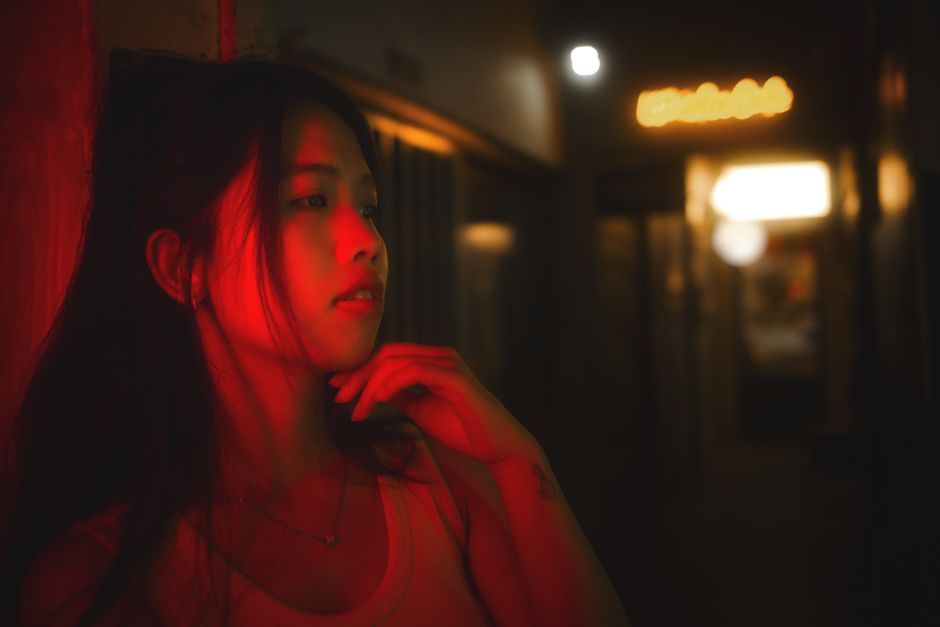 Stylized portrait of a woman under red neon light in a dimly lit corridor.