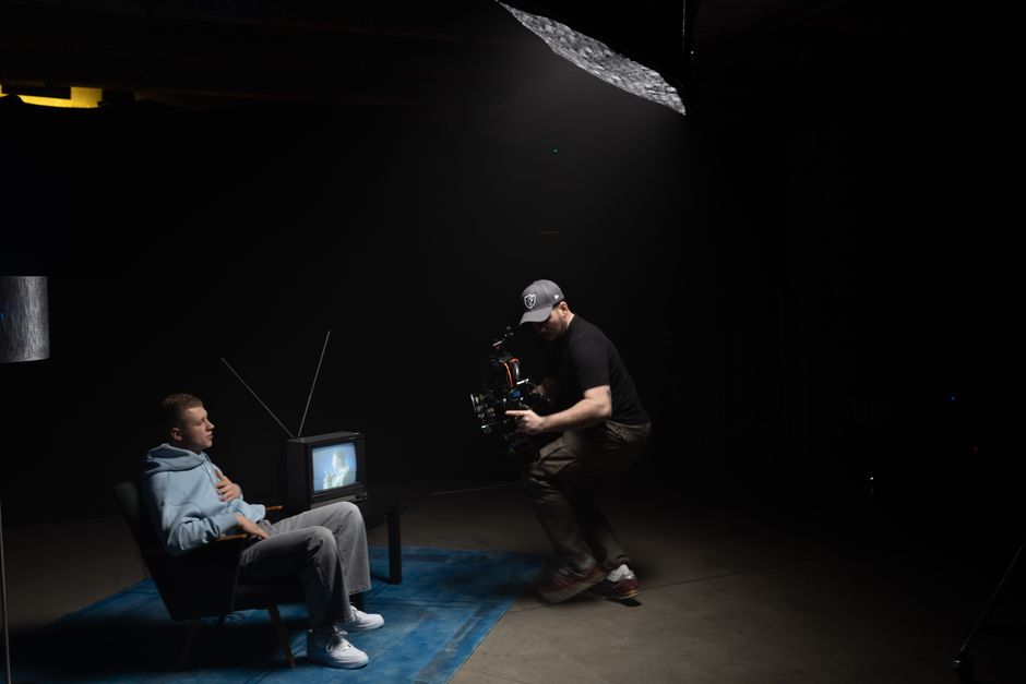A photographer captures a scene with a man sitting next to an old TV in a dimly lit studio.