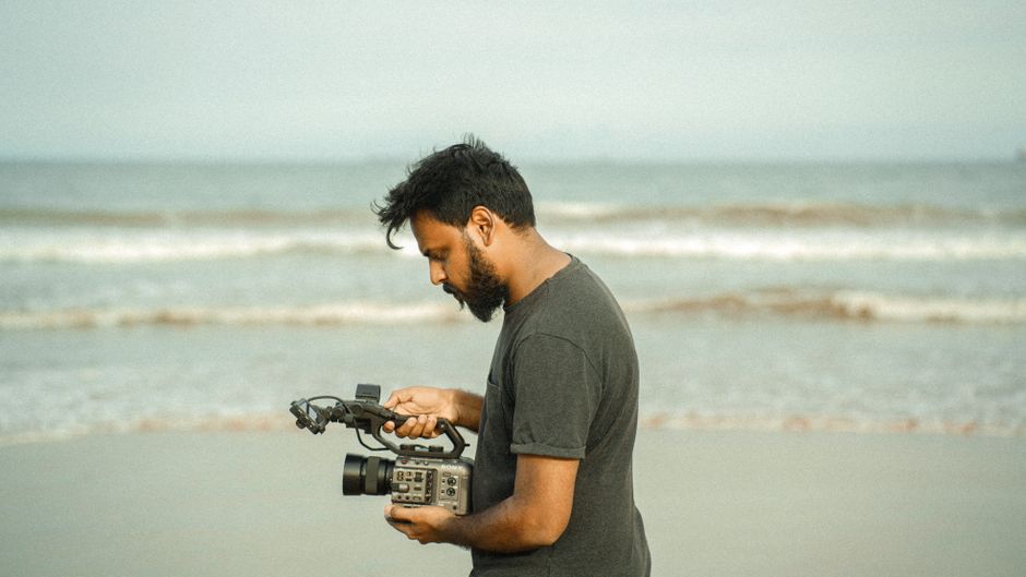 A young man holding a professional camera on the beach in Kakinada, India.