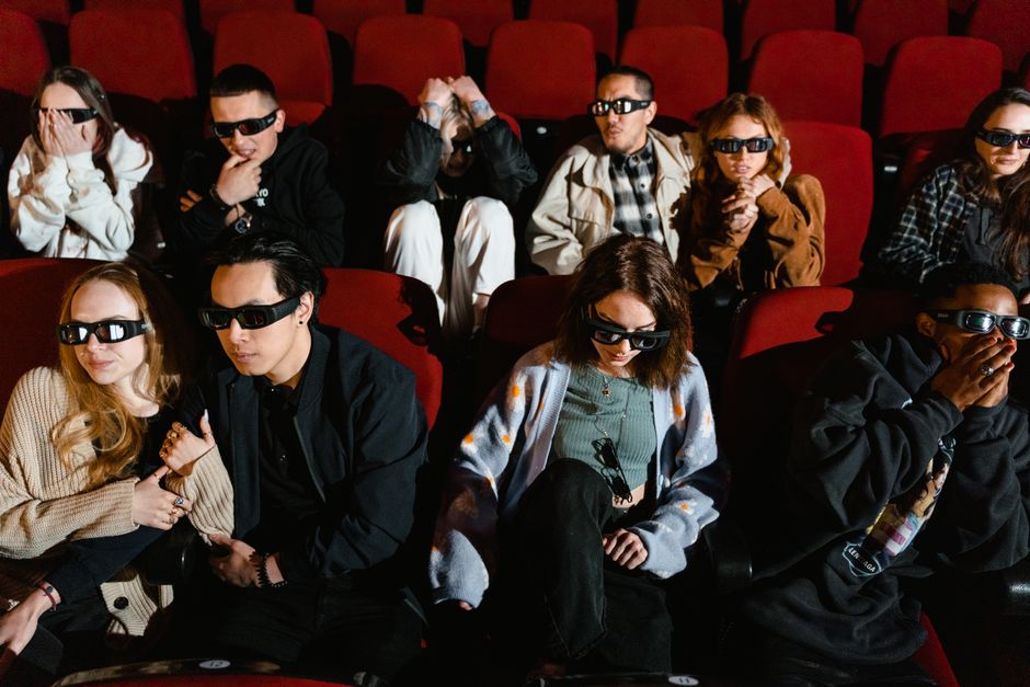 Group of people watching a movie in 3D glasses, expressing excitement and surprise.