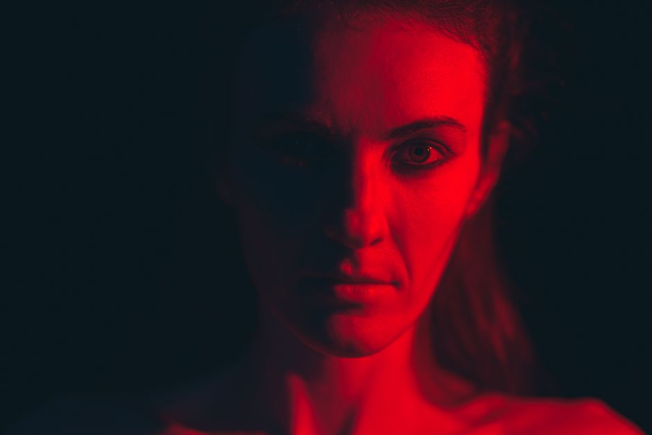 Close-up of a woman with serious expression illuminated by dramatic red lighting, creating an intense and moody atmosphere.