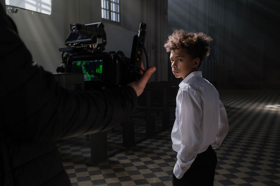 A young actor on a film set, captured in a cinematic moment with professional lighting and camera equipment indoors.