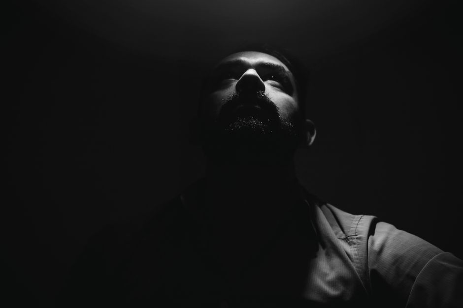 Moody grayscale portrait of a bearded man looking up with shadow play.