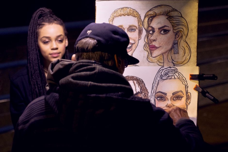 A street artist sketches a portrait of a woman during nighttime on an urban street.