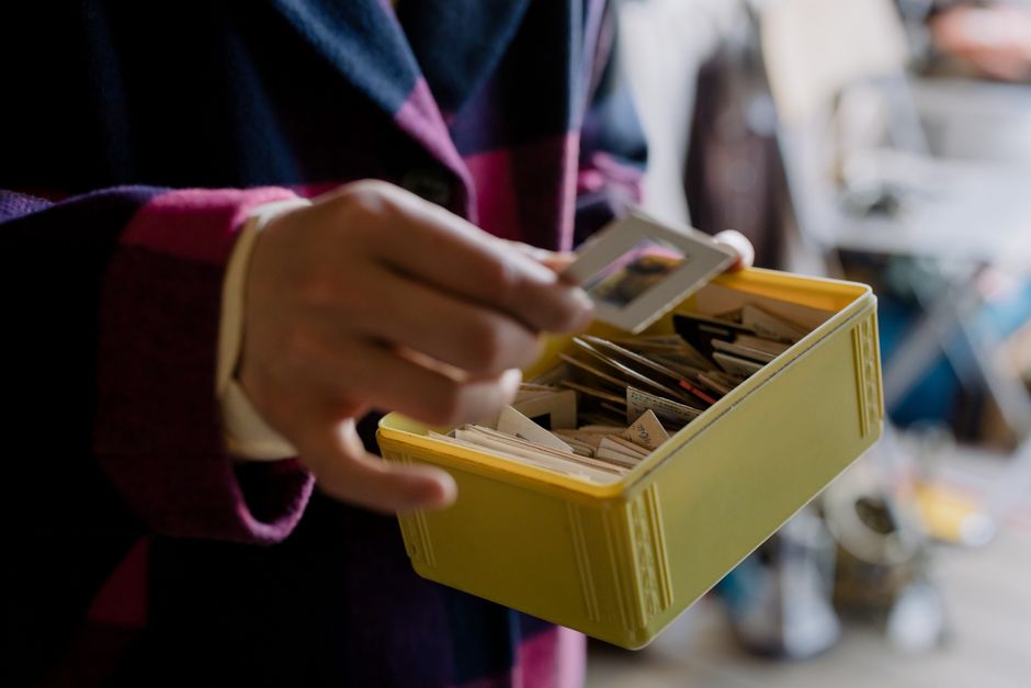 Close-up of a person examining old photo slides in a yellow box indoors.
