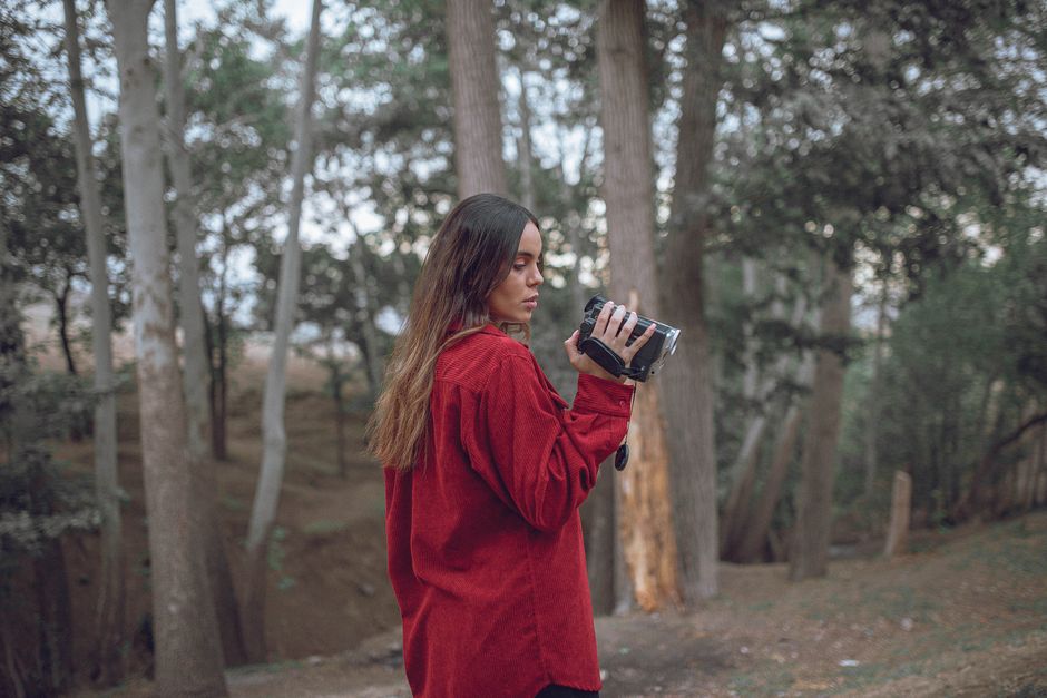 Young woman holding a camcorder in a serene forest, capturing nature sights.