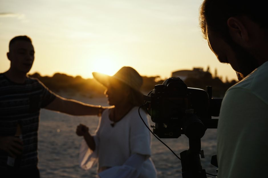 Silhouettes of people filming with camera and equipment on a beach during sunset.