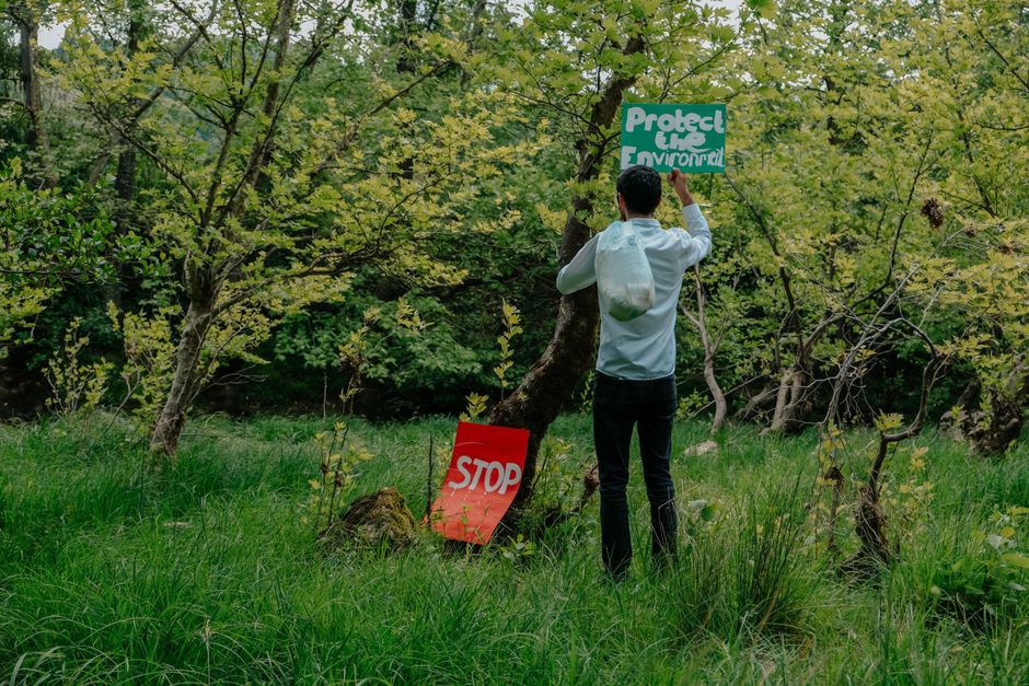 A man places a 'Protect the Environment' sign in a lush green forest.