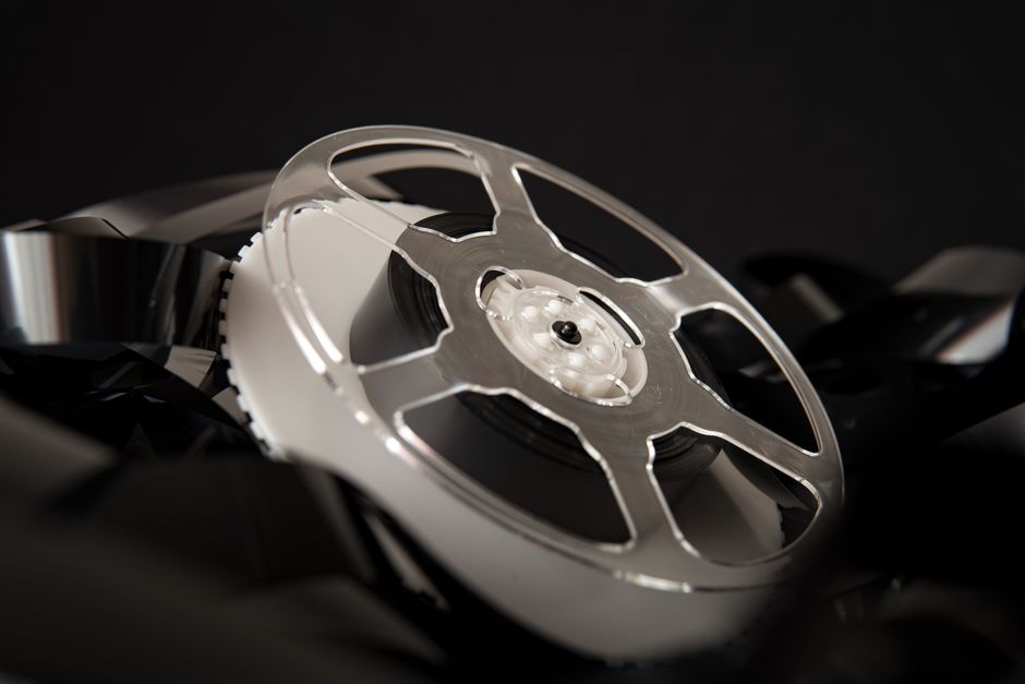 Transparent plastic bobbin placed on pile of unrolled film for movie production on black background