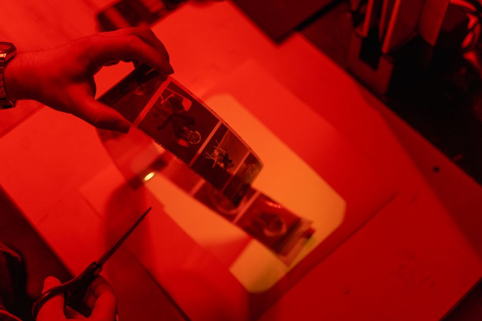 Hands cutting a filmstrip in a dimly lit darkroom, emphasizing film processing artistry.