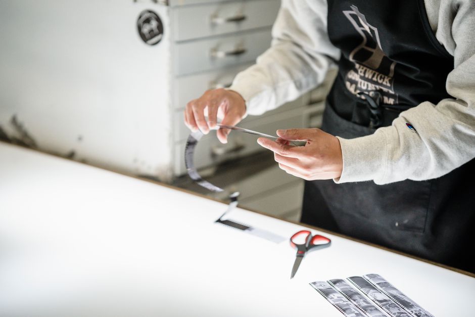 Photographer handles film negatives on a lightbox in a studio setting, showcasing film processing techniques.