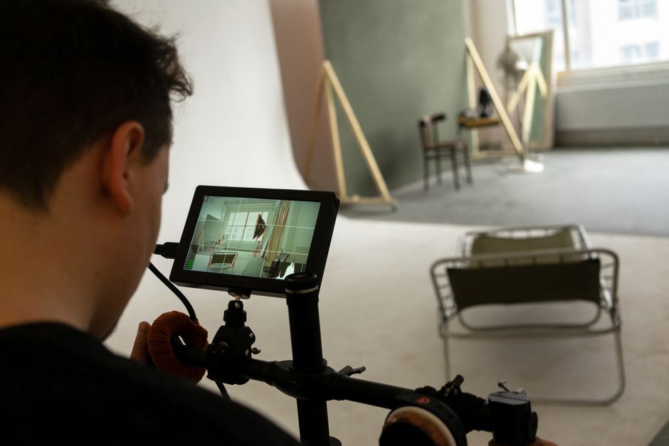 Back view of crop male with modern camera on tripod in blurred room with deckchair