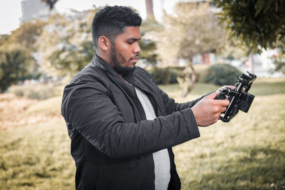 A man holding a camera rig, filming in an outdoor park setting in Lima, Peru.