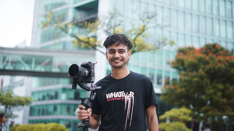 Portrait of a young filmmaker holding camera equipment outdoors in urban setting.
