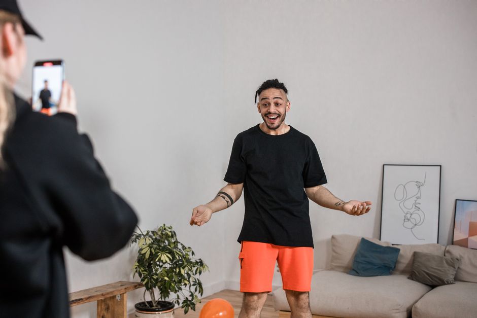 Man in black shirt vlogging indoors with smartphone capturing lively expressions.