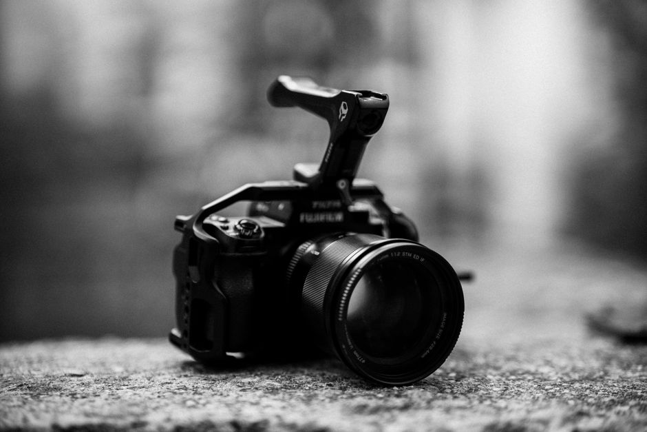 A close-up black and white image of a DSLR camera resting on a stone surface.