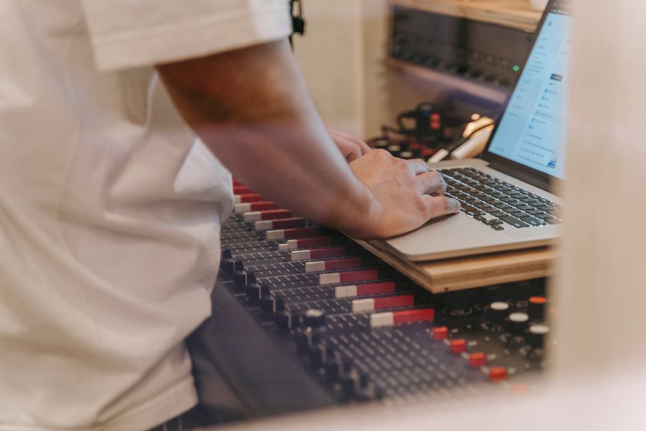 A person using a laptop on top of a sound mixer in a recording studio setting.